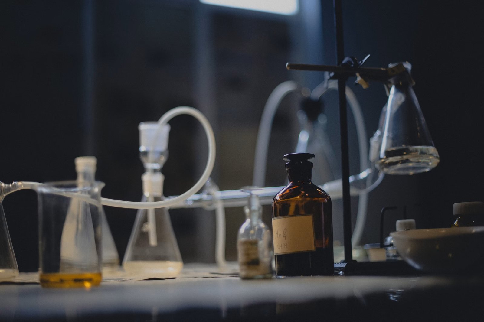 Laboratory glassware — flasks, tubing, and an amber reagent bottle — arranged on a dimly lit bench